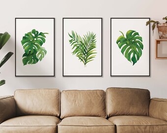 Könnte beinhalten: Drei gerahmte Drucke von tropischen Blättern, mit einem Monstera-Blatt, einem Farnwedel und einem weiteren Monstera-Blatt. Die Drucke hängen an einer weißen Wand über einem braunen Ledersofa.