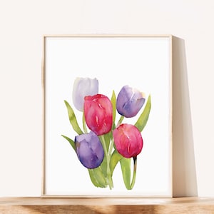 May include: Watercolor painting of a bouquet of tulips in shades of red, purple, and white, with green leaves. The artwork is framed in a light-colored wooden frame, set against a white background. A floral art print.