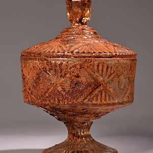 May include: A vintage glass candy dish with a lid, featuring a diamond pattern and a rust-coloured patina. The dish has a pedestal base.