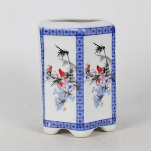 Puede incluir: Jarrón hexagonal de cerámica blanca con patrones geométricos azules y blancos y un diseño floral con pájaros rojos.