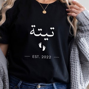 May include: Black t-shirt with white text that reads "Thiltha" in Arabic script, two white footprints, and "EST. 2022".