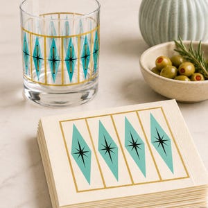 Op de afbeelding: Een helder drinkglas en een stapel crèmekleurige papieren servetten. Beide items zijn voorzien van een herhalend patroon van turquoise ruiten met zwarte sterren in het midden, omlijst door dunne gouden verticale lijnen.