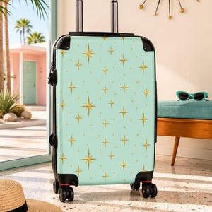 May include: A mint green hard-shell rolling suitcase featuring a repeating pattern of gold four-pointed stars. The luggage has a black frame, a retractable silver handle, and four black spinner wheels, providing a functional travel accessory.