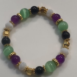 May include: A colourful beaded bracelet with green, purple, black, white, and gold beads. The beads are separated by gold-coloured spacers. The bracelet is designed to be worn around the wrist. The bracelet's beads are made of various materials.