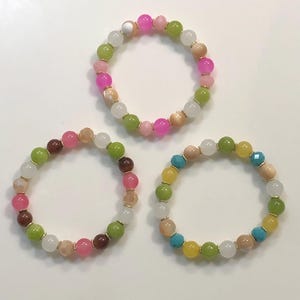 May include: Three colourful beaded bracelets with a mix of green, white, pink, yellow, brown and turquoise beads.
