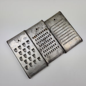 May include: Three vintage metal cheese graters with the word "RAPID" and "PAT. APPL'D FOR" printed on each. The graters have different sized holes.
