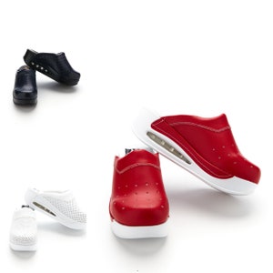 Puede incluir: Tres pares de zuecos de deslizamiento en blanco, rojo y azul marino. Los zuecos tienen una suela de plataforma blanca con un diseño texturizado. Los zuecos están hechos de cuero y tienen un diseño perforado.