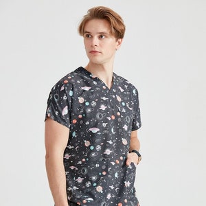 May include: A black short-sleeved scrub top with a V-neck and a pocket on the left side. The top features a colorful print of planets, stars, and other celestial objects.