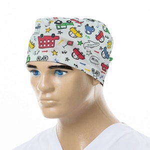 May include: A light grey surgical scrub cap featuring a colourful cartoon car and star pattern. The cap is worn by a mannequin. The cars are red, yellow, blue, and green. The cap is made of a soft, lightweight material.