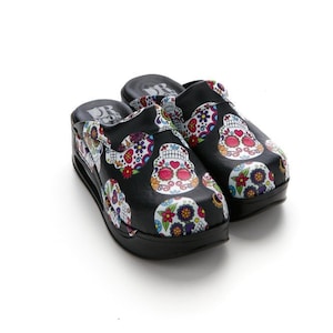 Puede incluir: Zuecos negros con fondo blanco y estampado de calaveras de azúcar de colores.
