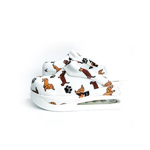 Puede incluir: Zapatillas blancas de deslizamiento con estampado de dachshund. Las zapatillas tienen una suela blanca gruesa.
