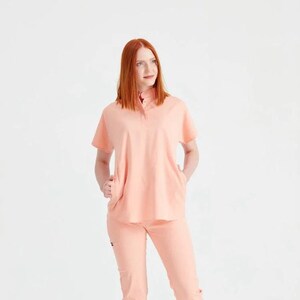 May include: A peach-colored scrub top and matching pants with a collared neckline and short sleeves.