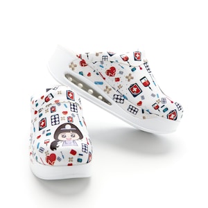 Puede incluir: Un par de zapatos blancos de deslizamiento con un tema médico. Los zapatos tienen una enfermera de dibujos animados y símbolos médicos impresos en ellos.