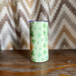 May include: A green and white stainless steel tumbler with a shamrock pattern. The tumbler has a lid and is perfect for holding beverages.