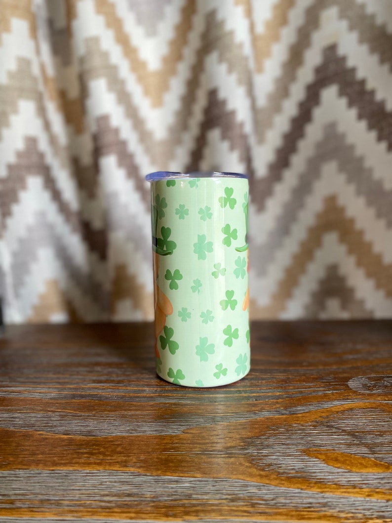 May include: A green and white stainless steel tumbler with a shamrock pattern. The tumbler has a lid and is perfect for holding beverages.
