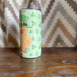 May include: A green and yellow tumbler with a cartoon image of a chick wearing a green leprechaun hat. The tumbler is covered in a pattern of green shamrocks.