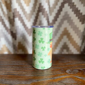 May include: A green and white stainless steel tumbler with a shamrock and leprechaun design. The tumbler has a lid and is perfect for holding beverages.
