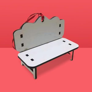May include: A miniature wooden bench with a white seat and back, outlined in black. The back has a cloud-like shape and a red ribbon for hanging. The bench has four black square cutouts on the seat and back, and black legs.