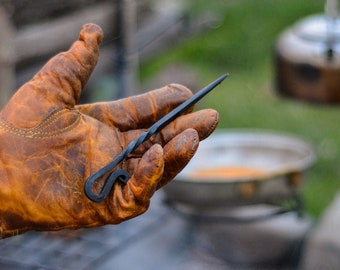 May include: A close-up of a hand wearing a brown leather glove holding a black metal fire poker with a twisted handle.