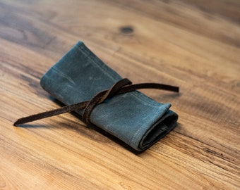 May include: A gray canvas roll-up pouch with a brown leather strap tied around it. The pouch is rolled up and tied with the strap.