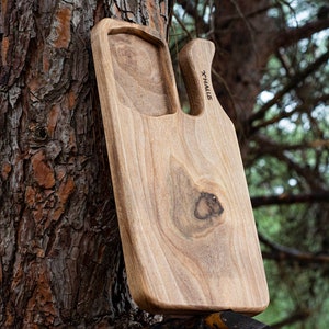Puede incluir: Una tabla de cortar de madera con una forma única y un asa. La tabla tiene un acabado de madera natural y está grabada con la palabra "X-HALLUS".