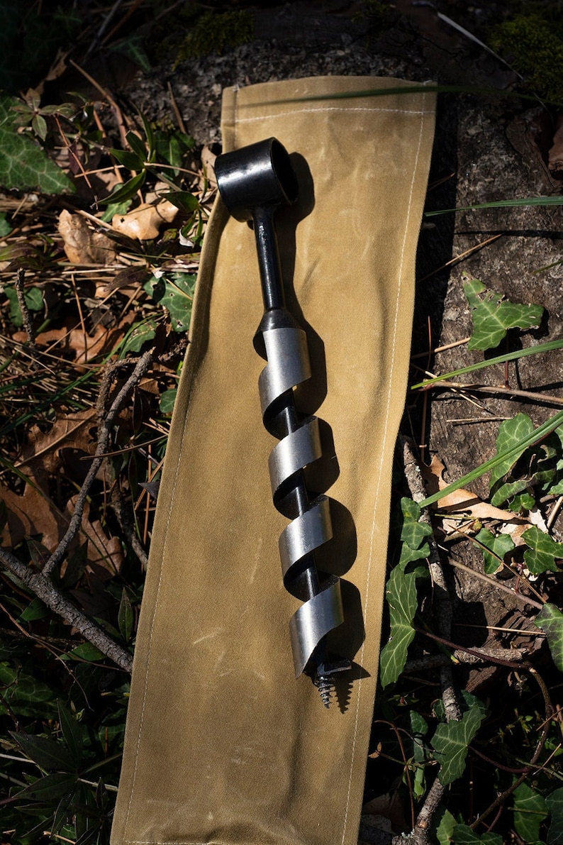 May include: A black and silver drill bit with a spiral design, lying on a brown canvas pouch.