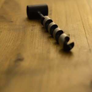 May include: A black and silver drill bit with a handle on a wooden surface.