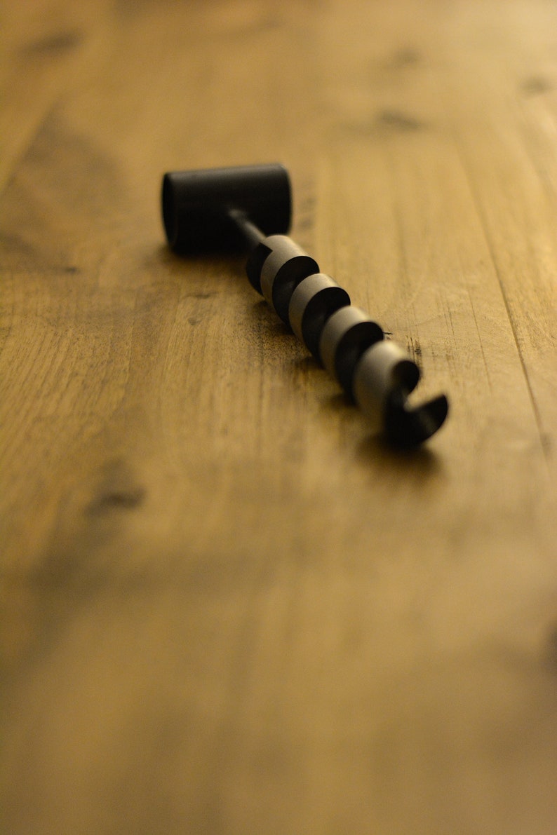May include: A black and silver drill bit with a handle on a wooden surface.