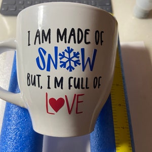 May include: White ceramic mug with black text that reads "I am made of snow but, I'm full of love" with a blue snowflake and a red heart.