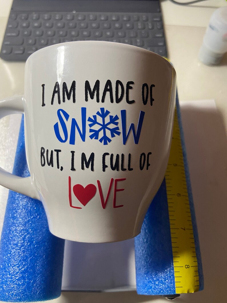 May include: White ceramic mug with black text that reads "I am made of snow but, I'm full of love" with a blue snowflake and a red heart.