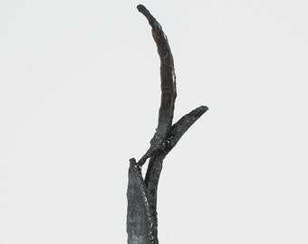 May include: Abstract metal sculpture with a dark, textured finish. The sculpture features a vertical design with curved and angular elements, resembling stylized plant forms. The piece stands on a rectangular base.
