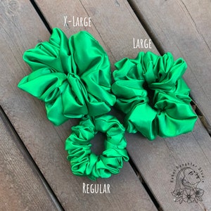 May include: Three green satin scrunchies in different sizes: X-Large, Large, and Regular. The scrunchies are arranged on a wooden surface.