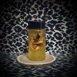 May include: A small glass bottle with a black lid filled with a yellow liquid and containing dried, light brown, organic material.