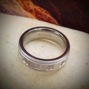 Peut inclure: Une bague en argent avec des chiffres romains grav&eacute;s sur le bord. La bague est en acier inoxydable.