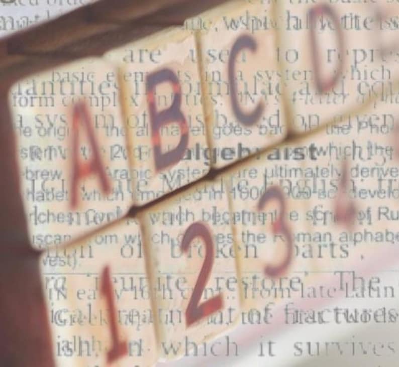 Peut inclure: Gros plan sur des blocs d'alphabet &eacute;pellant "ABC" et des blocs de nombres &eacute;pellant "123". Les blocs sont en bois et ont un aspect vintage. Les blocs sont pos&eacute;s sur une page de texte sur l'histoire de l'alphabet.
