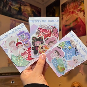 May include: Three packs of "Mystery Mini Bundle" stickers are held in a hand. Each pack features colorful stickers with cartoon characters, food, and text. The stickers have glitter accents and are on a white background.