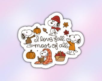 May include: A die-cut sticker featuring Snoopy in various autumn scenes with pumpkins, apples in a basket, and falling leaves. The text reads I love fall most of all in a cursive script. Snoopy wears a red hat and scarf, a brown jumper, and sits under a plaid blanket while reading a book.