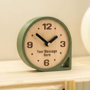 May include: A white ceramic mug with a black handle and the text "But First, Coffee" in a bold, black font. The mug is set against a blurred background, suggesting a cozy setting.