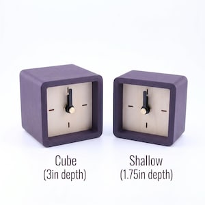 May include: Two square clocks with dark purple frames and light wood faces. The left clock is labeled Cube (3in depth) and the right clock is labeled Shallow (1.75in depth). Both clocks feature black hands and a gold center pin on the face.