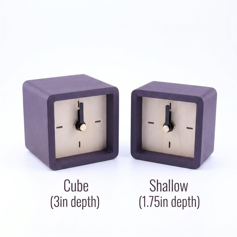 May include: Two square clocks with dark purple frames and light wood faces. The left clock is labeled Cube (3in depth) and the right clock is labeled Shallow (1.75in depth). Both clocks feature black hands and a gold center pin on the face.