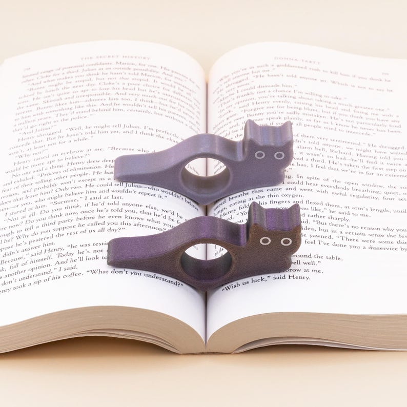 Metallic purple and silver cat thumb book page holders with bookmark, ergonomic and playful design, perfect gift for book lovers, adds charm to reading, ideal for birthdays, anniversaries, or as a stocking stuffer, a practical and adorable reading companion