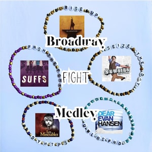 May include: Four beaded bracelets with different Broadway show album covers and titles. The bracelets are purple, gold, black and white, and blue. The titles are "Rise Up", "FNSHTHEOFGH", "Seize The Day", and "UWLBEFNDID".