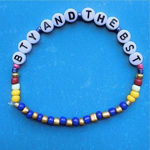 May include: A white beaded bracelet with the words "BTY AND THE BEST" spelled out in black letters. The beads are interspersed with yellow, red, and blue beads.
