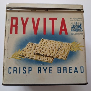 May include: A vintage tin box for Ryvita Crisp Rye Bread. The box is white with blue and red accents. The front of the box features a stack of two crispbreads and the text "RYVITA Crisp Rye Bread". The box also includes a royal crest and the text "By Appointment to the Late King George VI."