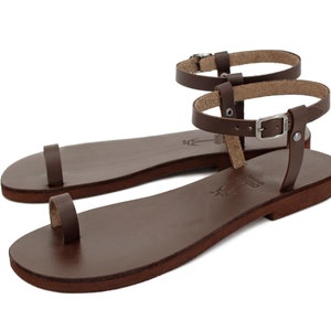 May include: Brown leather sandals with an ankle strap and buckle closure. The sandals have a simple design and are made of high-quality leather.