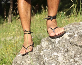 May include: A pair of black leather sandals with ankle straps. The sandals are tied around the ankles and have a simple design.