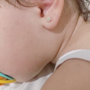 May include: A close-up of a baby's ear with a small, white flower-shaped earring.