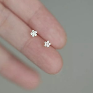 May include: A pair of small, delicate flower-shaped earrings with clear cubic zirconia stones.