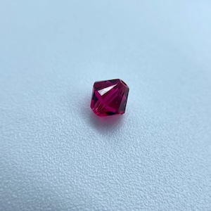 May include: A single, faceted, dark red glass bead.
