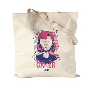 May include: A white canvas tote bag with a pink and blue illustration of a girl wearing a virtual reality headset. The text "GAMER GIRL" is printed below the illustration.